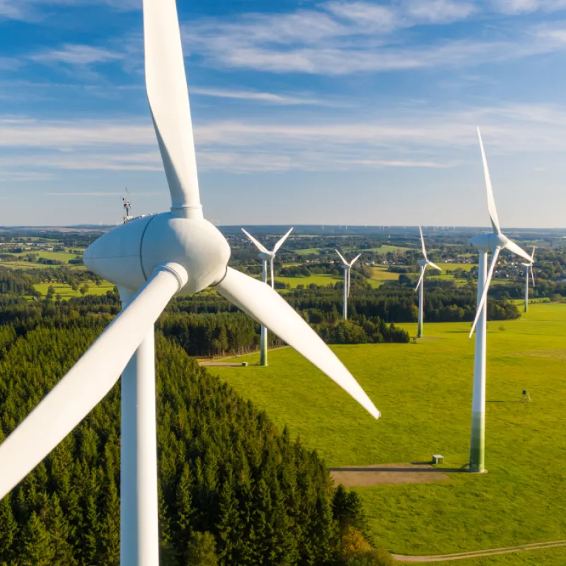 A close-up view of a windmill, representing sustainable energy generation, with a windmill park in the background, highlighting the eco-friendly and renewable power source